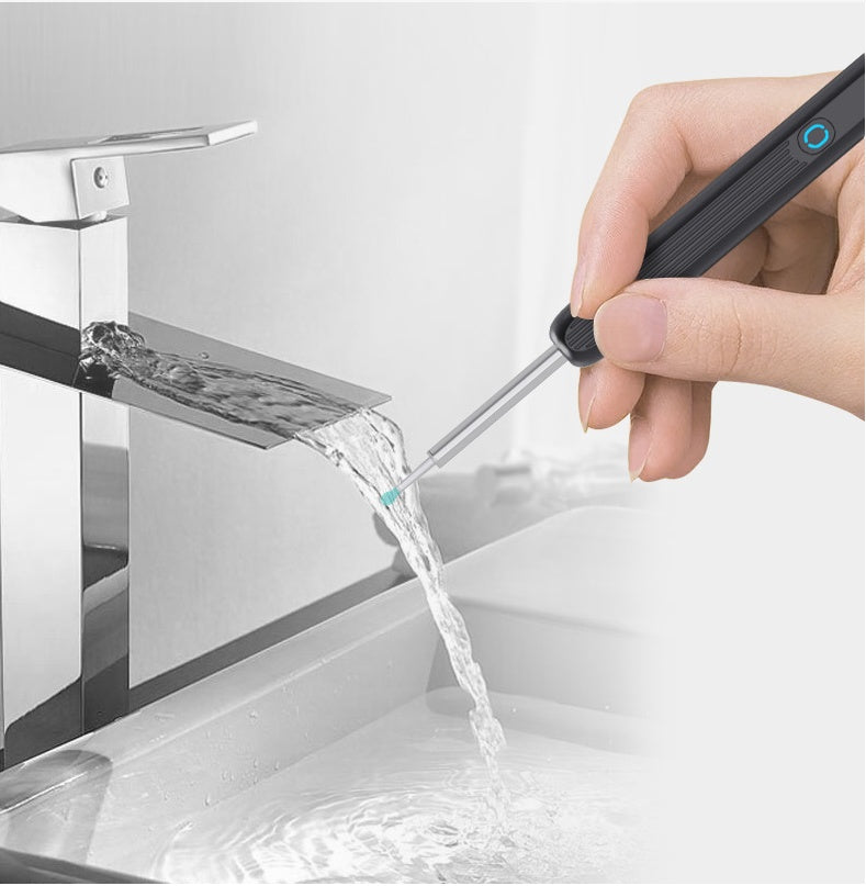 Hand holding an electronic ear picker with camera, with water flowing from a faucet into a sink