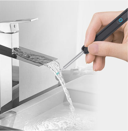 Hand holding an electronic ear picker with camera, with water flowing from a faucet into a sink